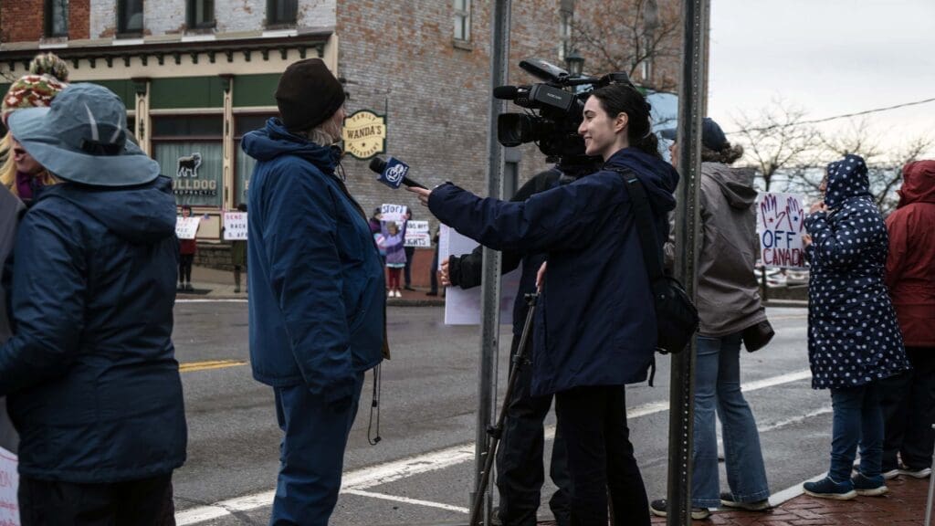 Reporter interviews protestor on street during demonstration.