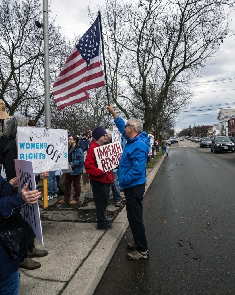 Protesters holding signs and an American flag.