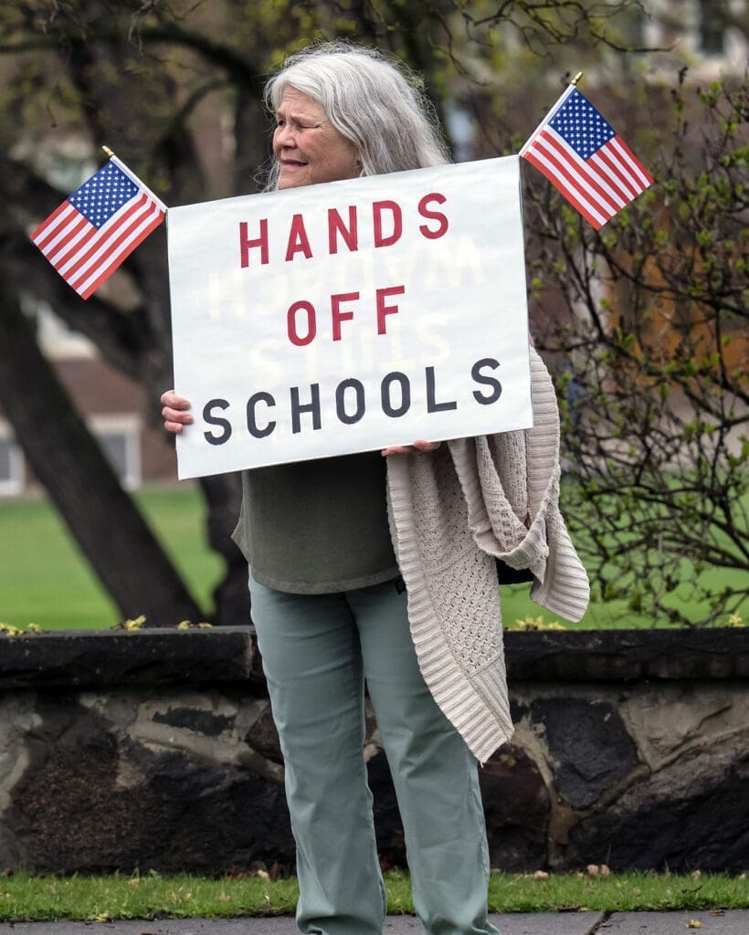 Protestor holds 'Hands Off Schools' sign with flags.