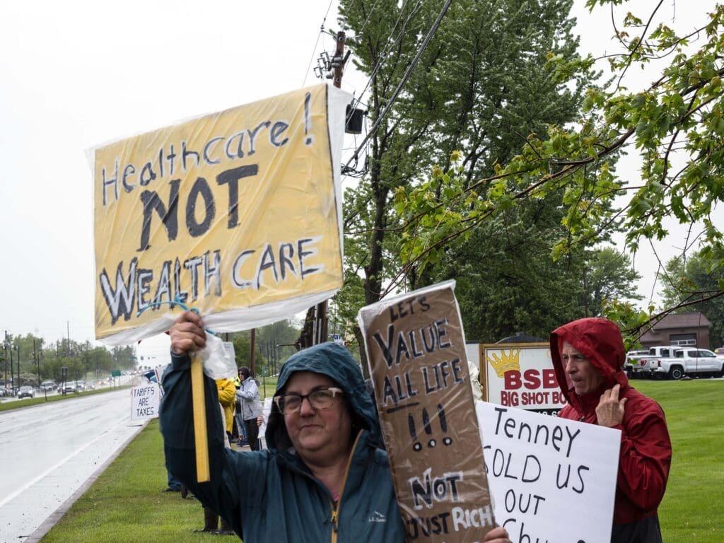 Protesters holding healthcare signs in the rain.