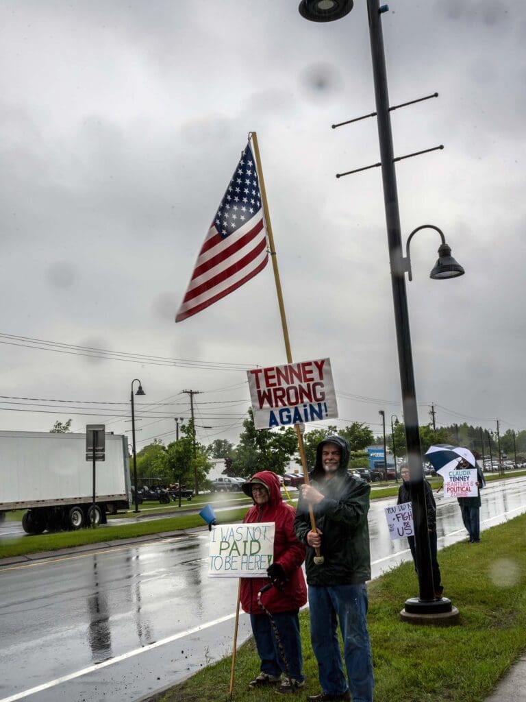Protesters in rain with anti-politician signs in street.