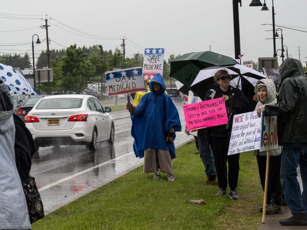 Protesters holding save Medicare and Medicaid signs in rain.