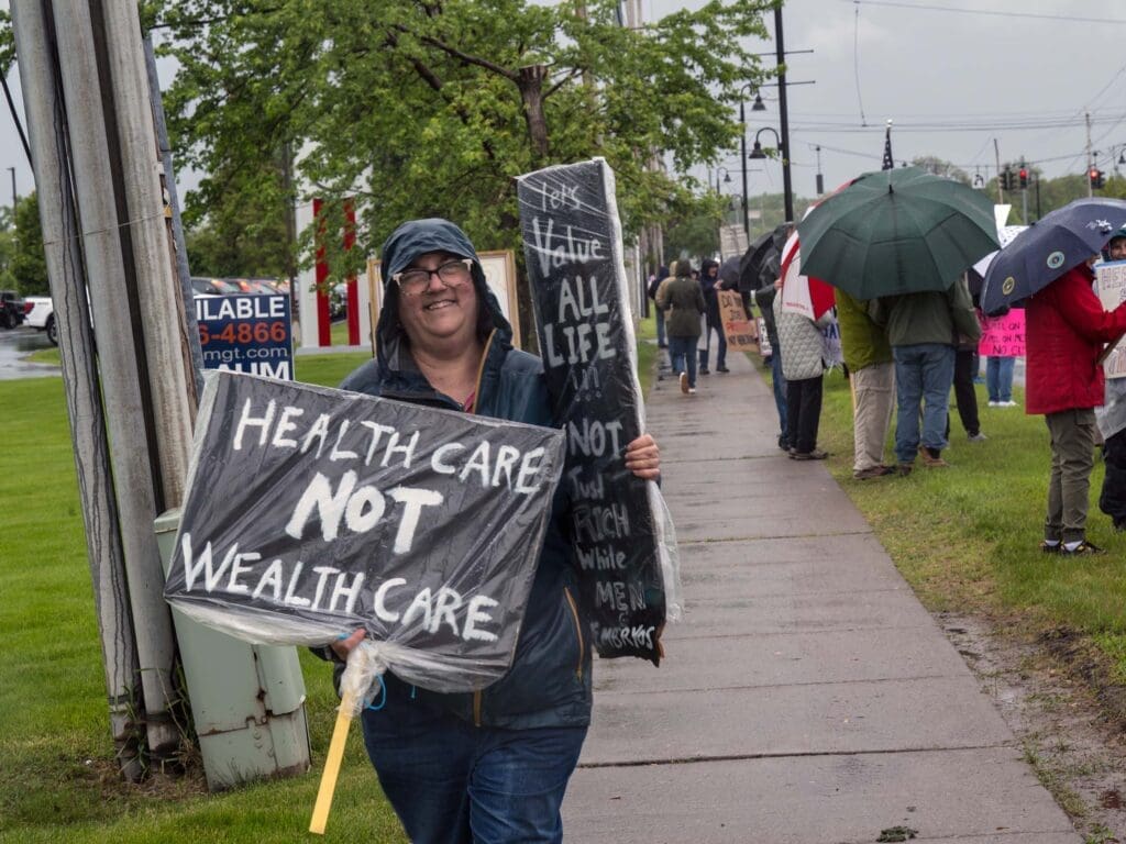 Protester holding sign for healthcare reform in rain.