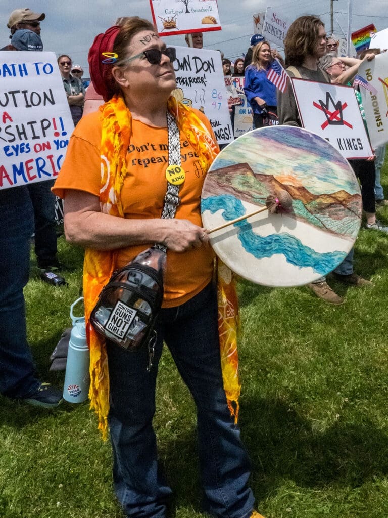 Protester with drum at rally holding signs.