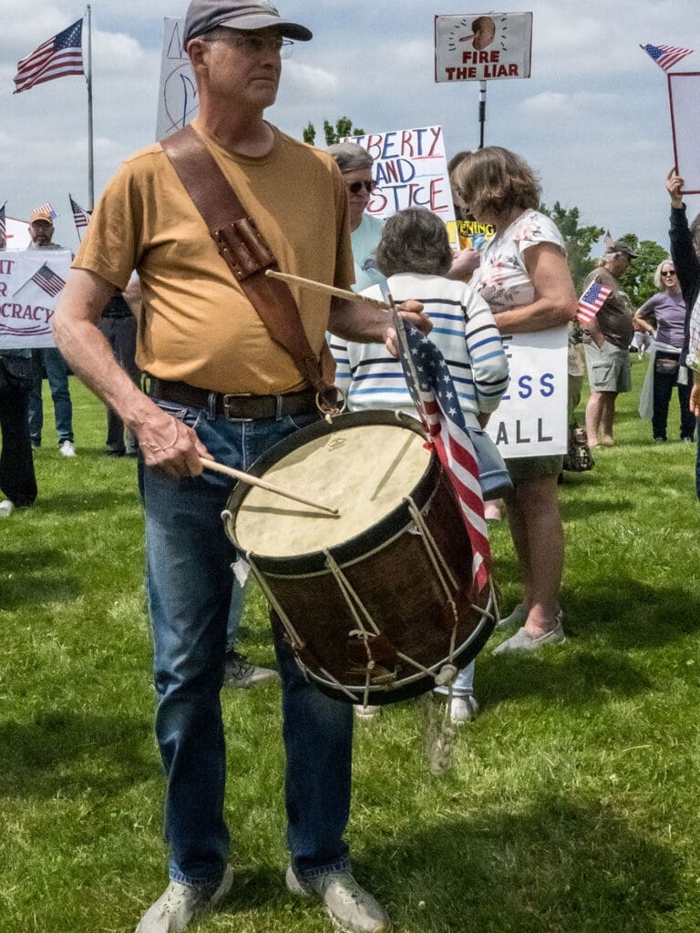Man with drum at protest with signs and flags.