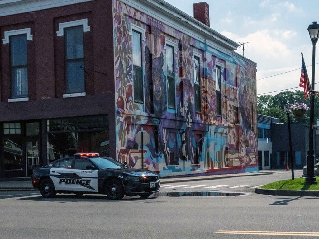 Police car near colorful mural on building wall.