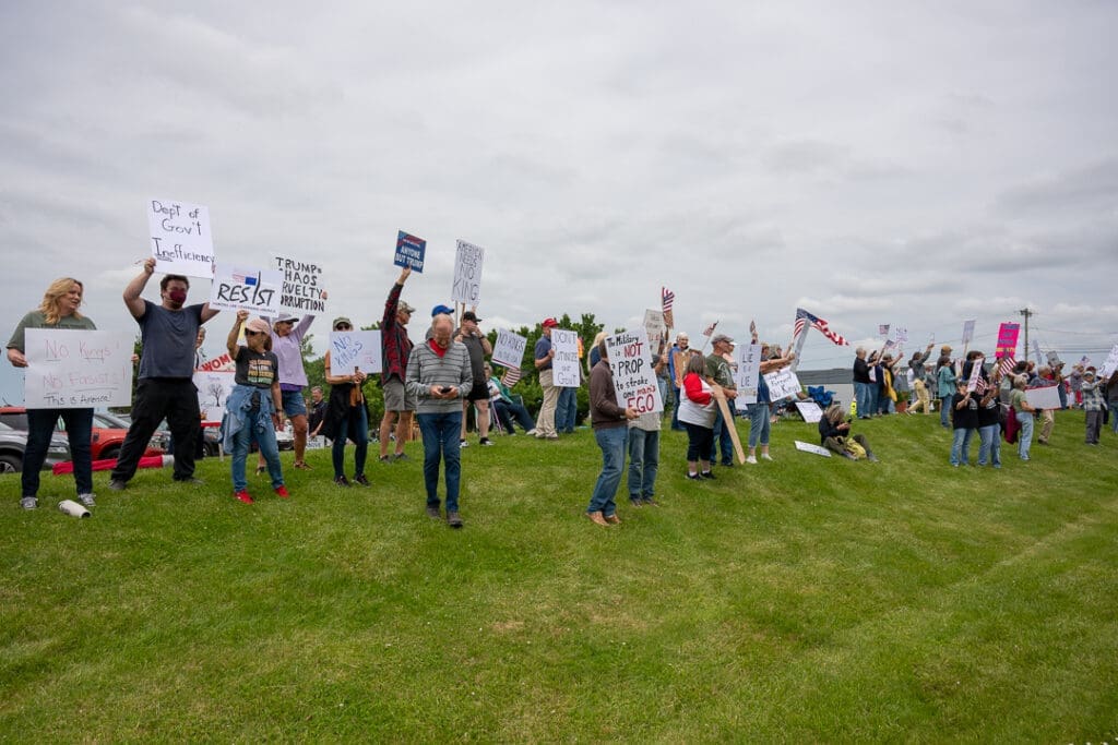 Protesters holding anti-government signs on grassy field.