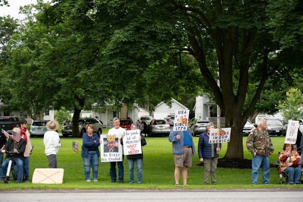Protesters holding signs on grassy area.