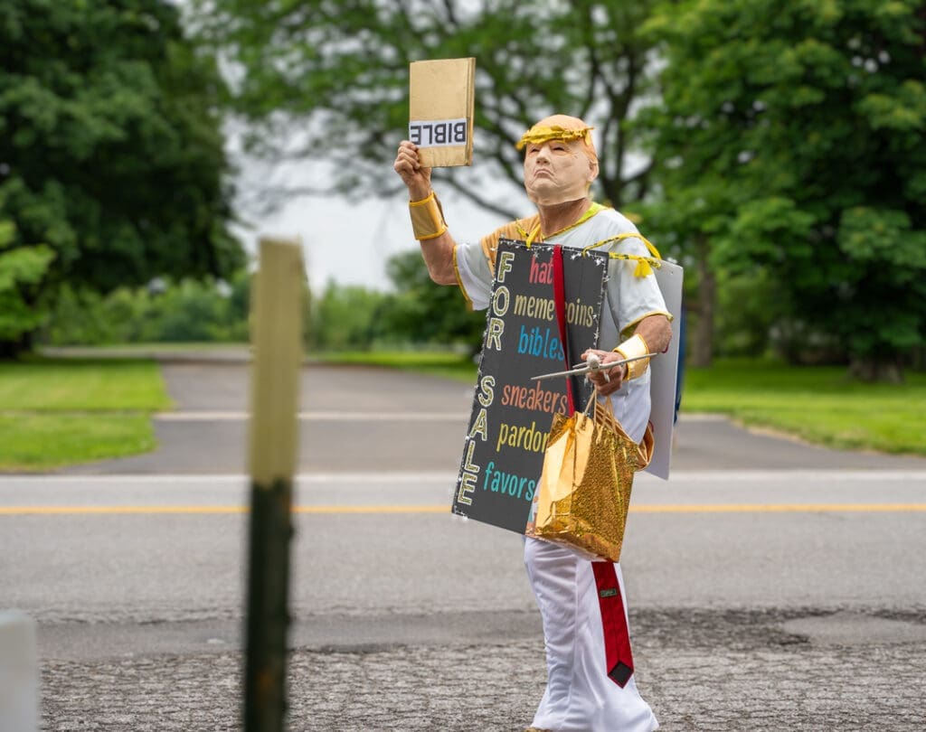 Person holding Bible sign and 'for sale' board outdoors.