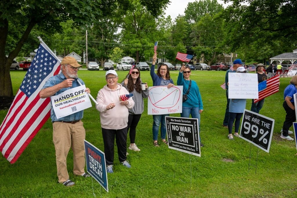 People holding protest signs in a park gathering.