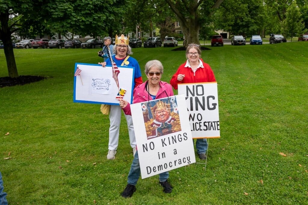 Protest with 'No Kings' signs at park.