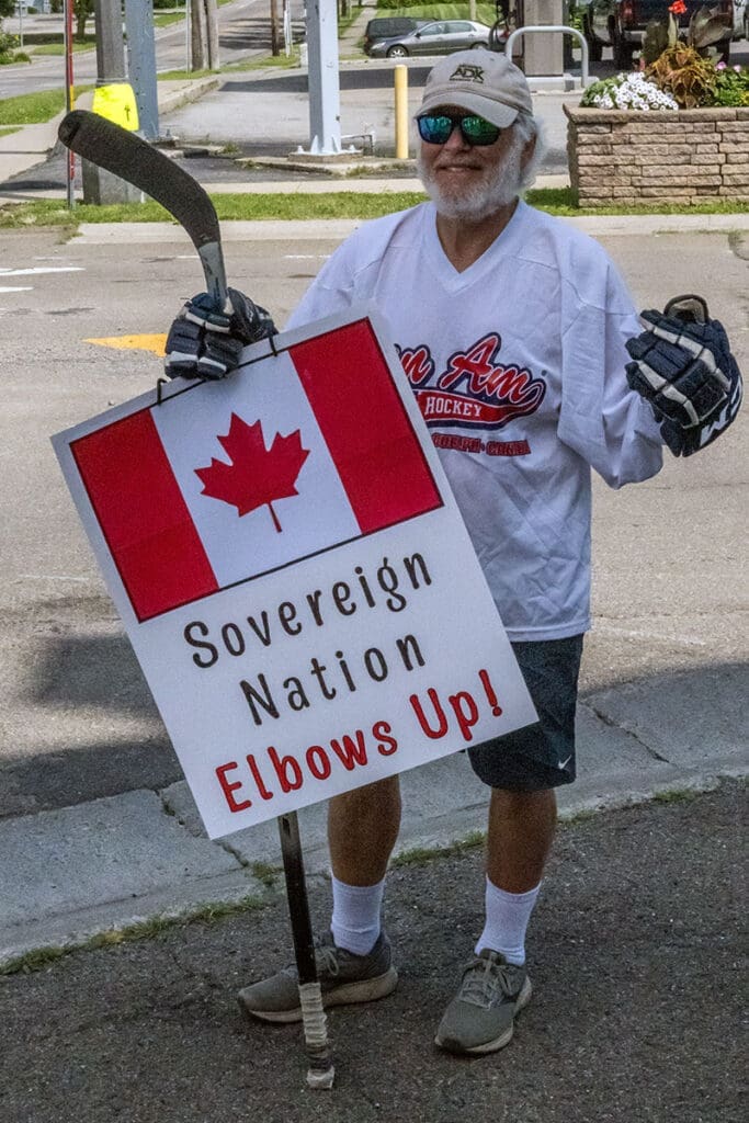 Man with hockey sign, Canadian flag, wearing gloves.