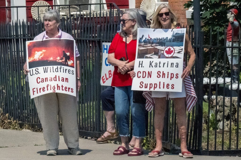 Three women holding signs about Canadian aid efforts.