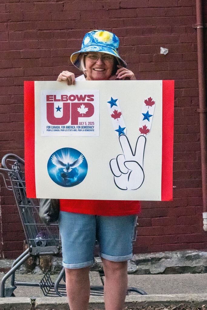 Smiling person holding Elbows Up poster for democracy.