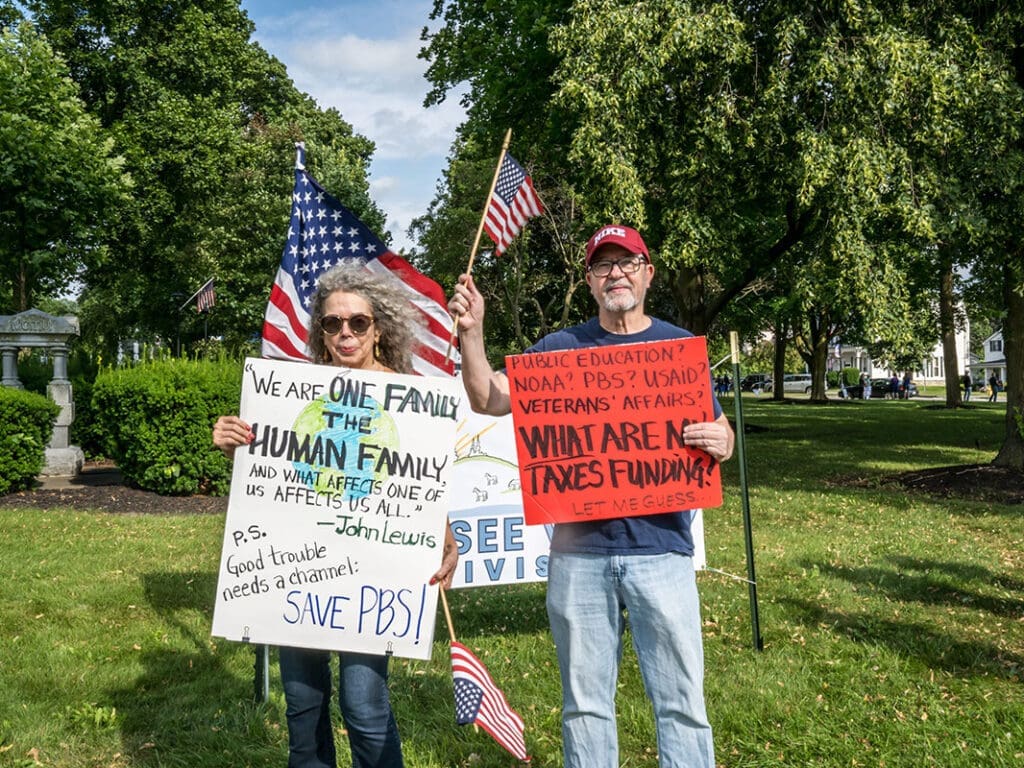 Two people holding protest signs in a park.