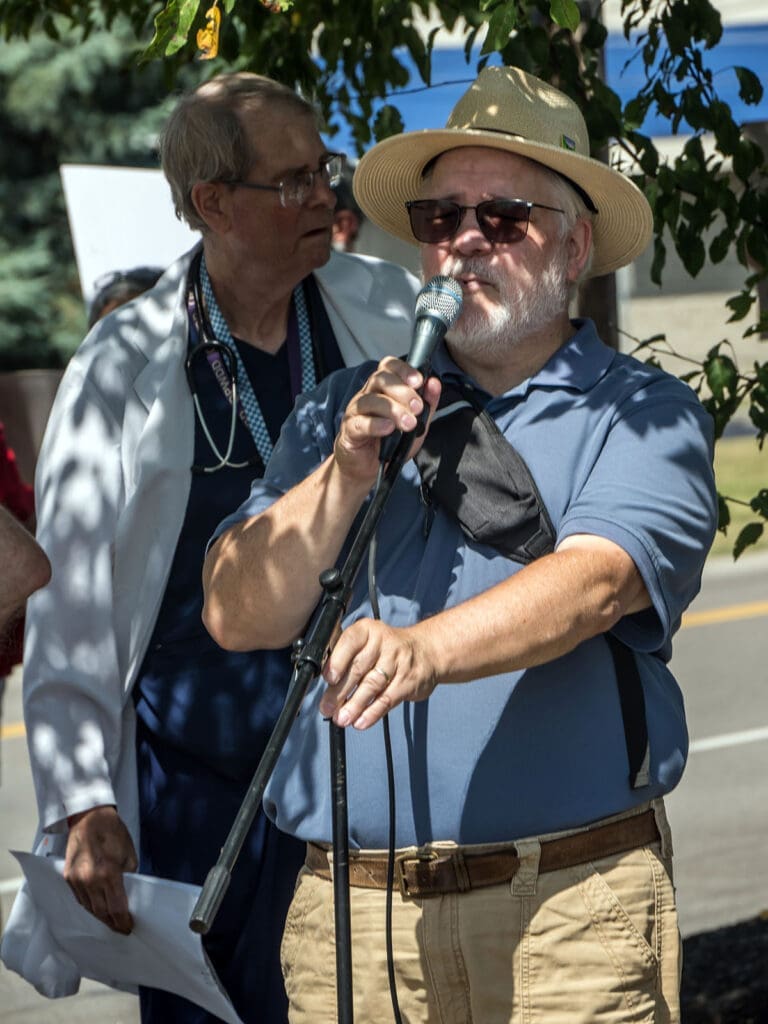 Man speaking at outdoor event with microphone.