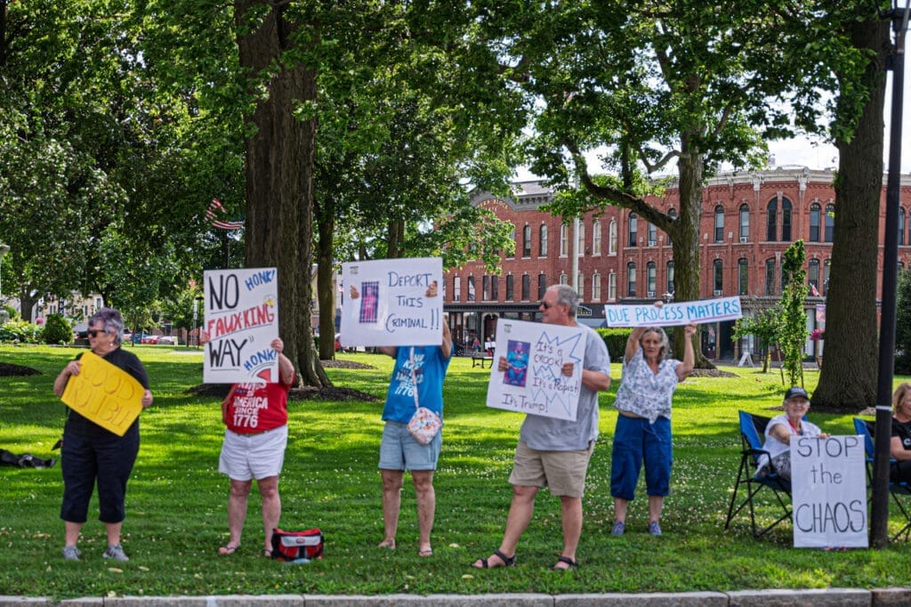 Protestors hold signs in park near historic buildings.