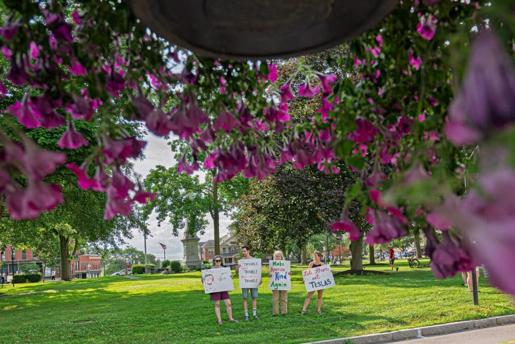 Group holding protest signs in park under flowers.