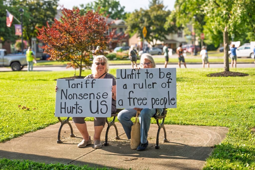 Two people protest with written signs on a bench.