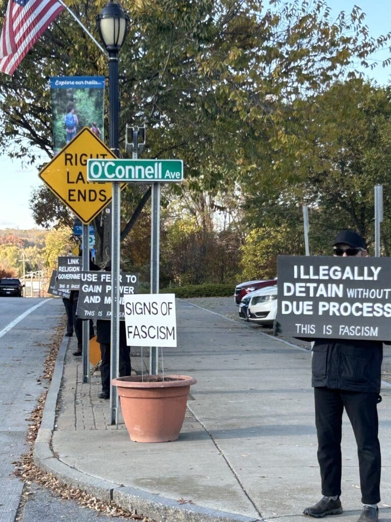 Protesters holding signs against fascism on sidewalk.