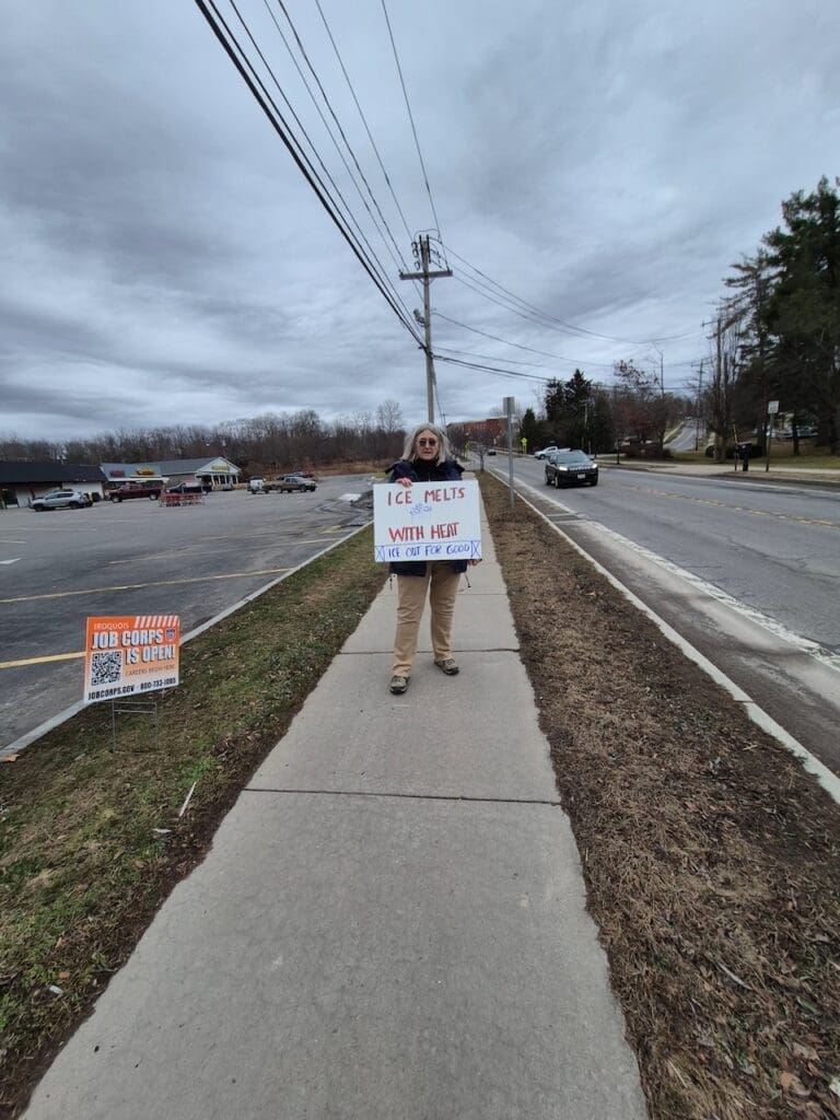 Person holding protest sign on sidewalk.