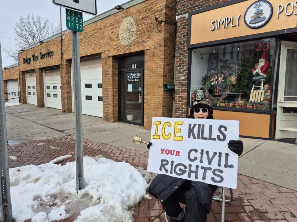 Protester holds sign against ICE outside storefronts.