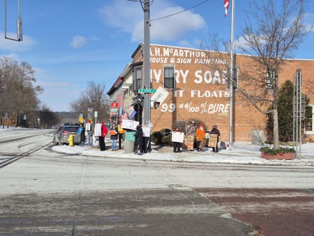 Protesters with signs stand on snowy street corner.