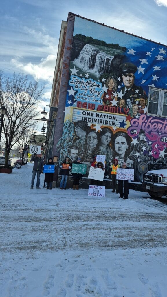 People holding signs in front of patriotic mural.