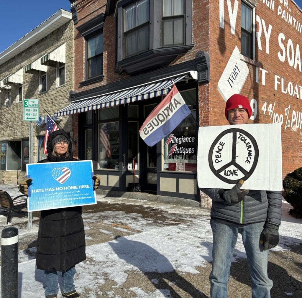 Protesters holding anti-hate and peace signs outside store.