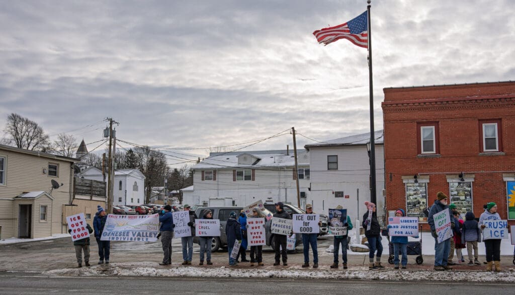 Protesters holding signs against ICE in a snowy town.