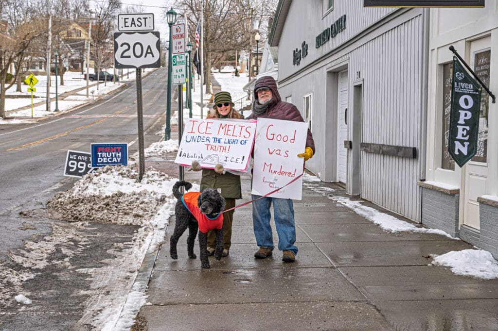 Protesters with signs and dog on snowy sidewalk.