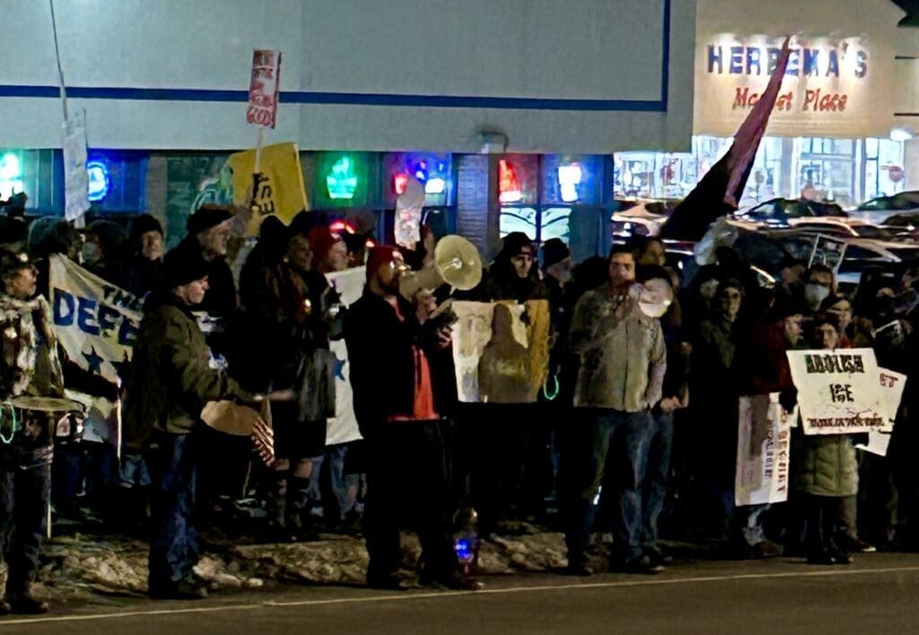 Night protest with signs outside a marketplace.