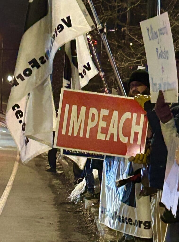 Protesters holding 'Impeach' signs at night rally.