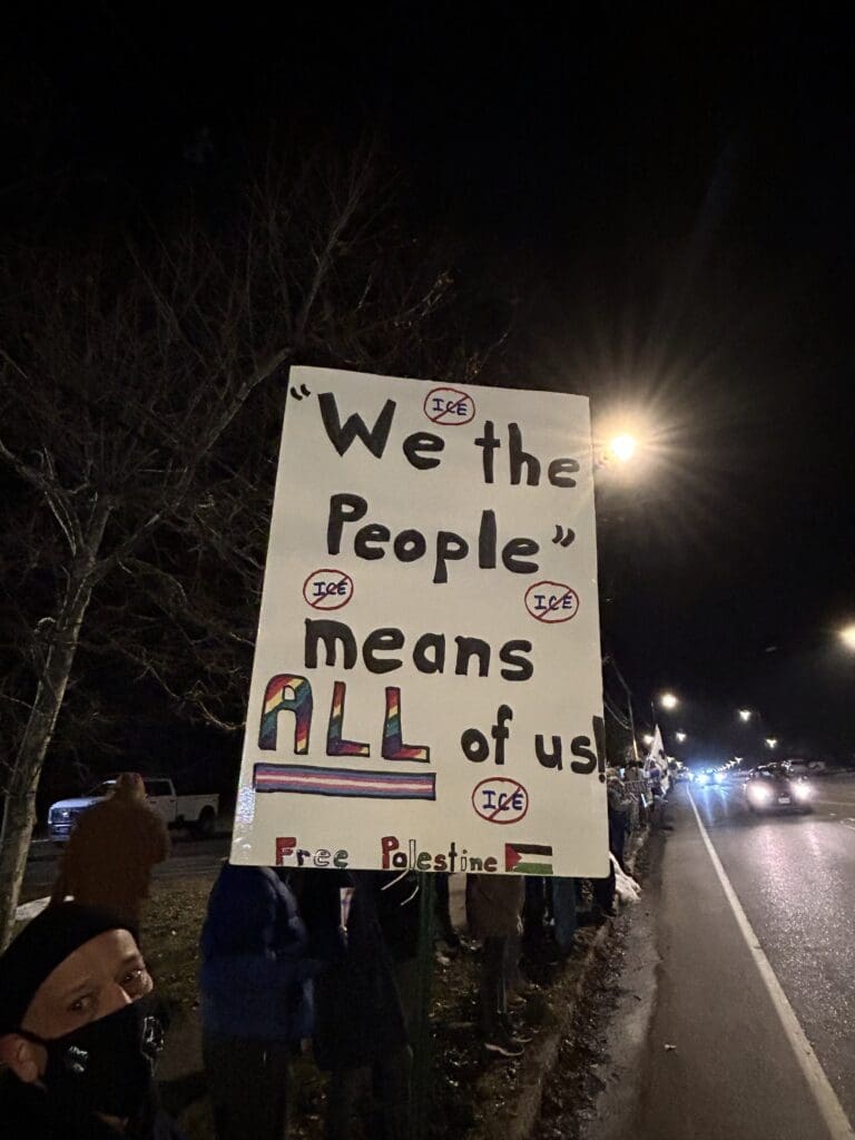 Protester holding 'We the People' sign at night.