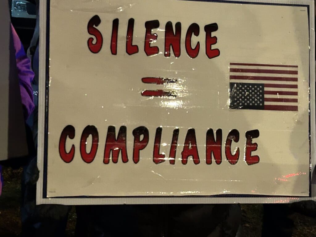 Protest sign: Silence equals compliance, American flag.