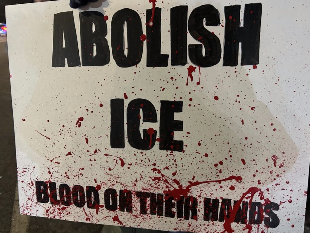 Protest sign reading 'Abolish ICE' with red splatters.