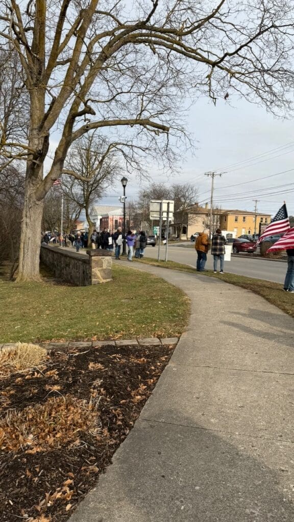 People gathered on sidewalk with flags and signs.