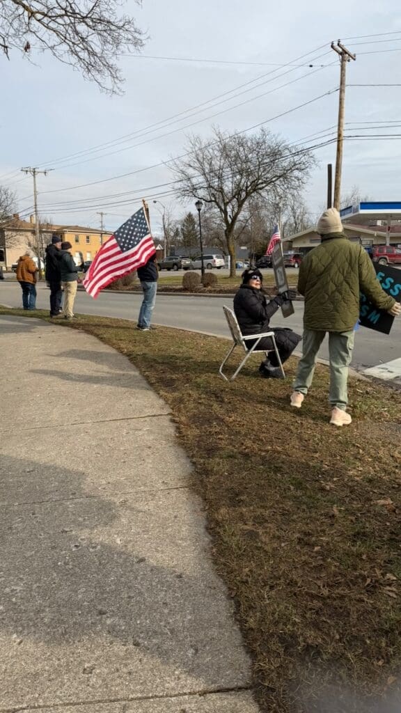 People holding American flags at roadside protest.