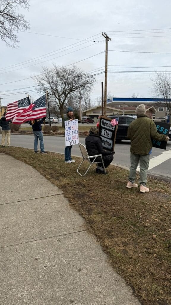 Protesters holding signs and flags on roadside.