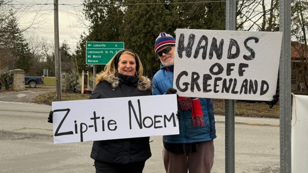 Protesters holding 'Hands Off Greenland' signs on roadside.