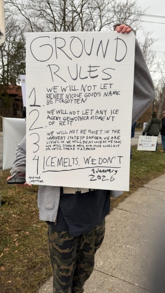 Person holding ground rules protest sign outdoors.