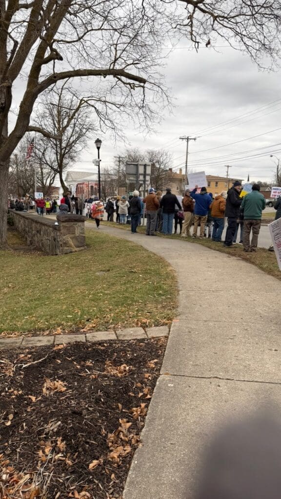 Crowd gathers for outdoor protest with signs.