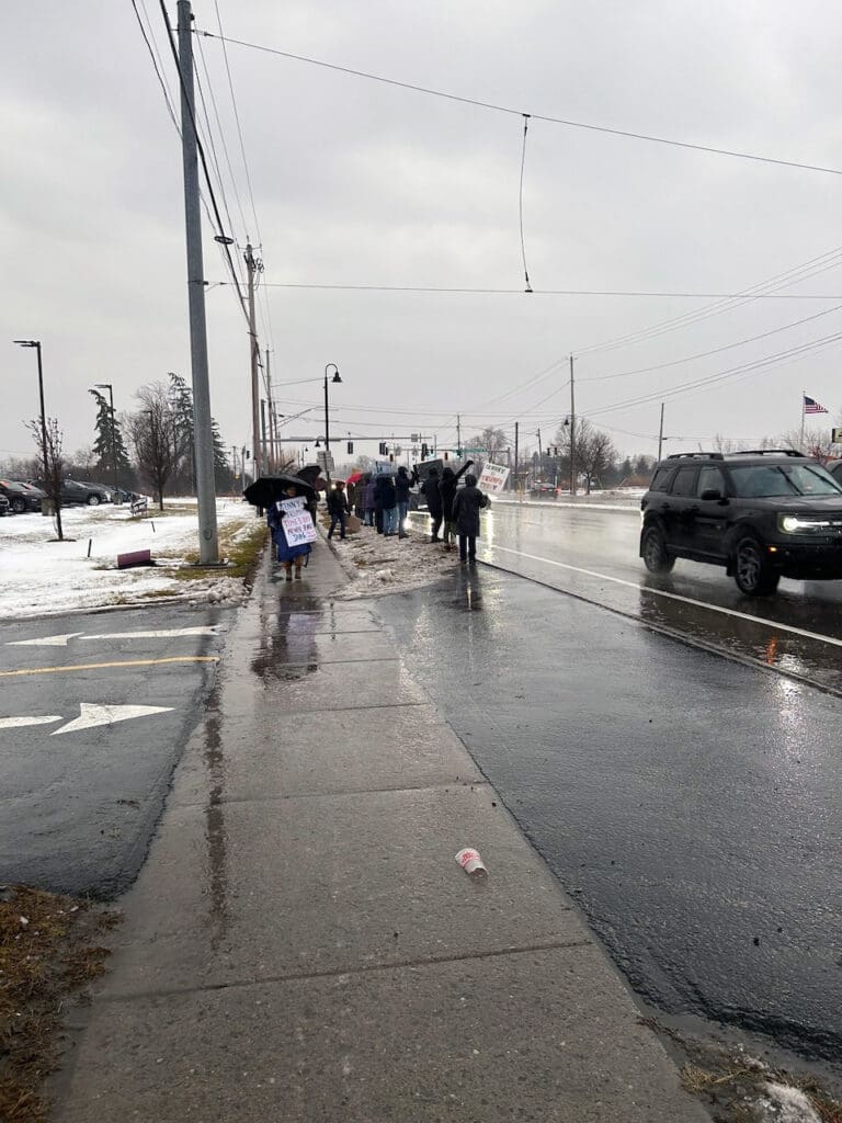 People protest on a rainy street with signs.