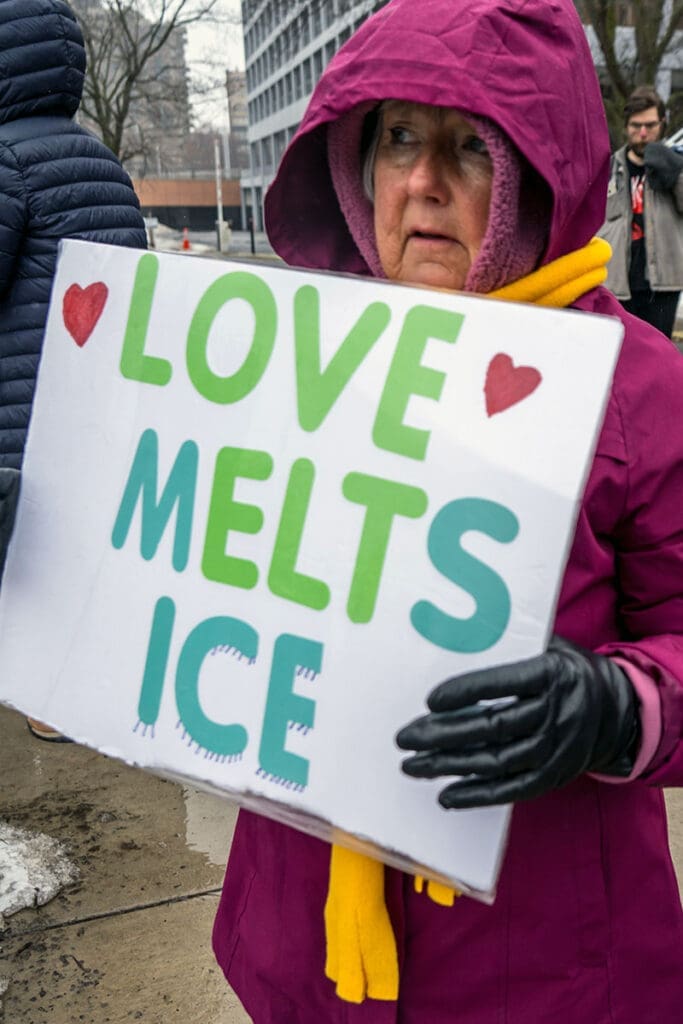 Person holding sign: 'Love Melts Ice' during protest.