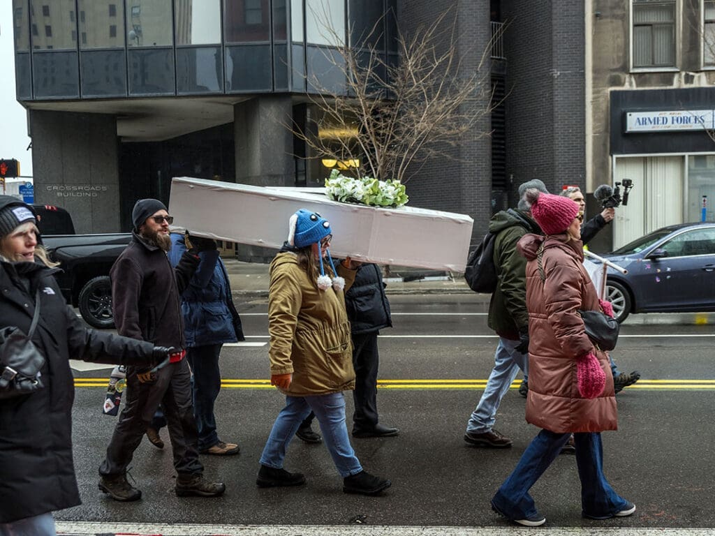 Group carrying large white box in city street.