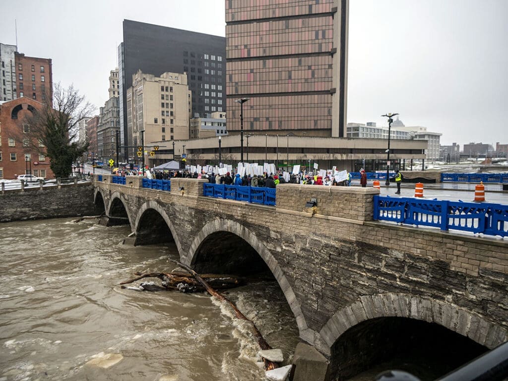 Busy urban bridge with river and buildings in background.
