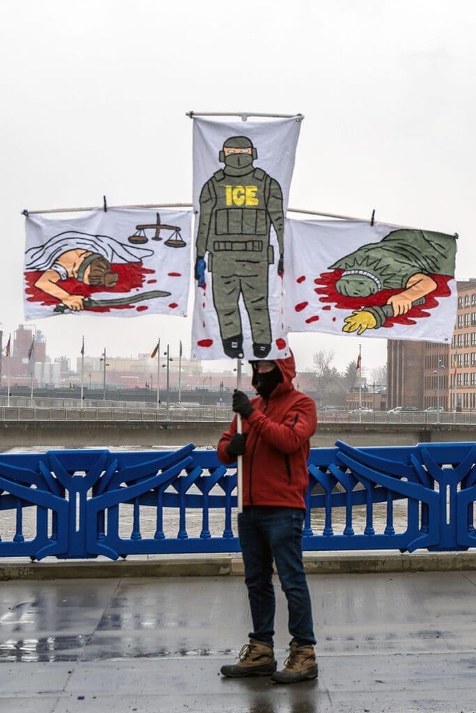 Protester holds banner against ICE on bridge.