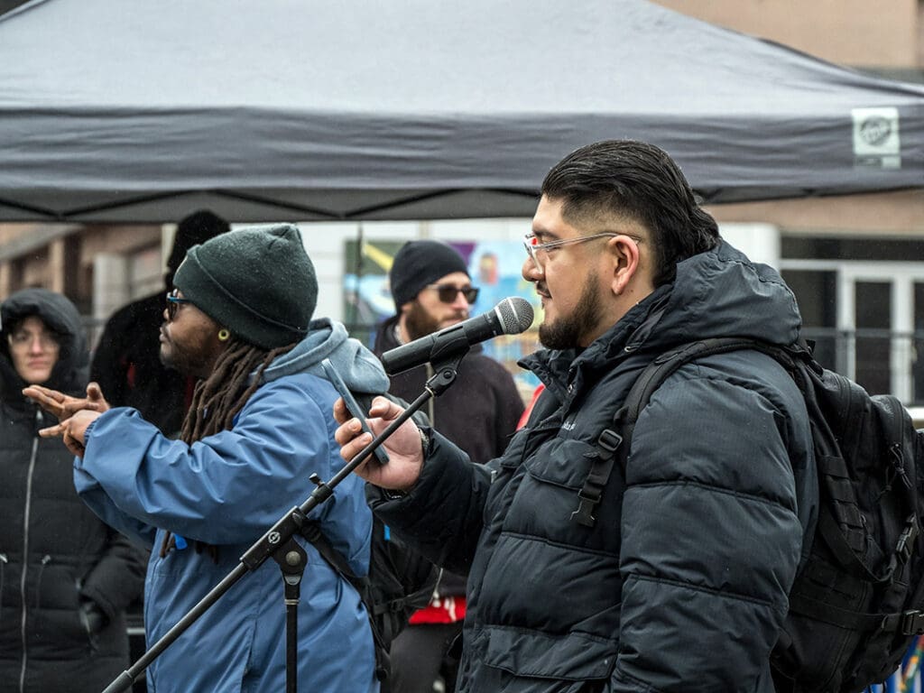 Man speaking into microphone outdoors in cold weather.