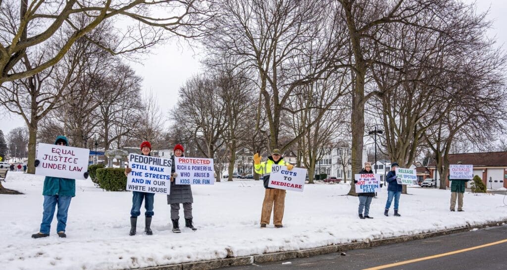 Protestors holding signs in snowy park, winter demonstration.