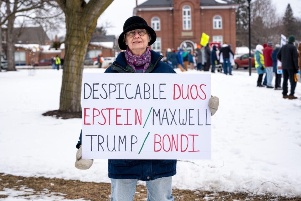 Protester holding sign against controversial figures in snow.